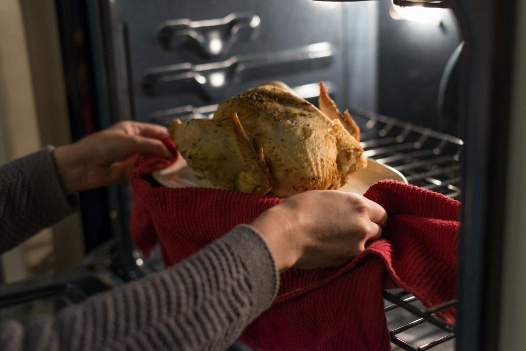 a roasted chicken is being pulled from an oven with a red towel being used to grab the platter