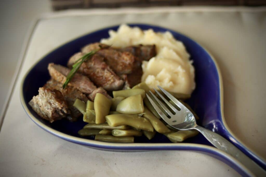 American Blue Brookline Skillet Plate with a fork resting on the handle; the plate is loaded up with a steak, potatoes, and green beans